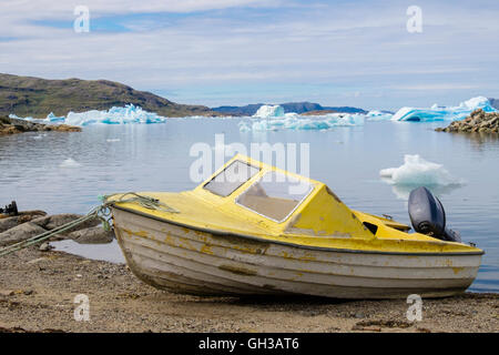 Kleine gelbe Fischerboot, gestrandet in Qajaq Hafen mit Eisberge schwimmen vor der Küste im Sommer. Narsaq Kujalleq Südgrönland Stockfoto