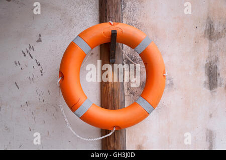 Eine orange Rettungsring hängen an einem hölzernen Pfosten gegen eine Steinmauer. Stockfoto