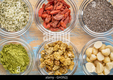 Superfood abstrakt - Hanfsamen, Gojibeeren, Chiasamen, Matcha Teepulver, Maulbeeren und Macadamia-Nüssen - Draufsicht des Glases Stockfoto