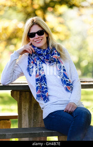 Niedrigen Winkel im Hochformat eine blonde Frau auf einer Parkbank sitzen und Lächeln, New Jersey, USA Stockfoto