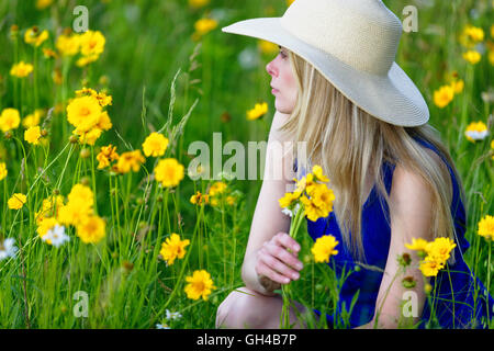 Close Up Blick auf eine junge Frau im Sommer Kleid und Hut in eine Wildflower kniend gefüllt, Wiese und Blumen halten Stockfoto