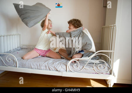 Kleinen Bruder und Schwester inszeniert eine Kissenschlacht auf dem Bett im Schlafzimmer. Unartige Kinder schlagen einander Kissen. Sie mögen t Stockfoto