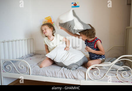 Kleine Jungen und Mädchen inszeniert eine Kissenschlacht auf dem Bett im Schlafzimmer. Unartige Kinder schlagen einander Kissen. Sie mögen das ki Stockfoto