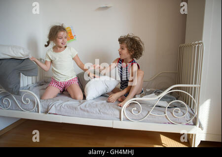 Kleine Jungen und Mädchen inszeniert eine Kissenschlacht auf dem Bett im Schlafzimmer. Unartige Kinder schlagen einander Kissen. Sie mögen das ki Stockfoto