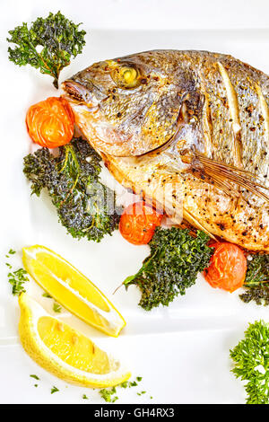 Vergoldete Kopf Brassen Fisch auf einem weißen Teller mit gegrillten Tomaten, Grünkohl und grob gekörnte Salz geröstet. Stockfoto