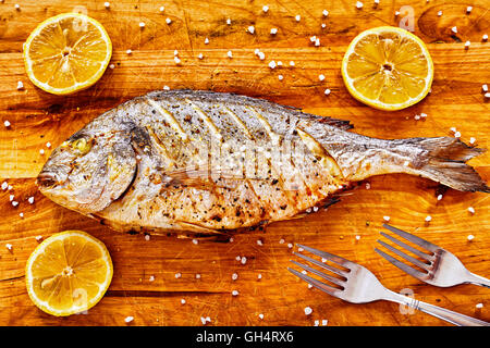 Vergoldete Kopf Brassen Fisch auf einem Holztisch mit Zitronen und Meersalz gekörnt geröstet. Stockfoto