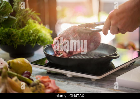 Hand hält Fleisch mit einer Zange. Stockfoto