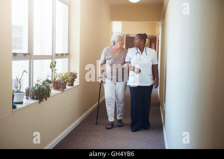 In voller Länge Portrait von senior Frau zu Fuß mit ihrer Krankenschwester im Pflegeheim. Medizinische Arbeit hilft Patientin. Stockfoto