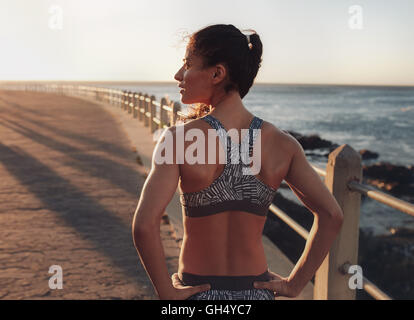 Hintere Ansicht Bild Fitness Frau in Sportbekleidung stehend an einer Strandpromenade entfernt am Abend. Sportlerin mit wegschauen Stockfoto