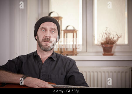 Mann mit Gitarre und hat eine Gitarre halten und sitzen vor einem Fenster Stockfoto