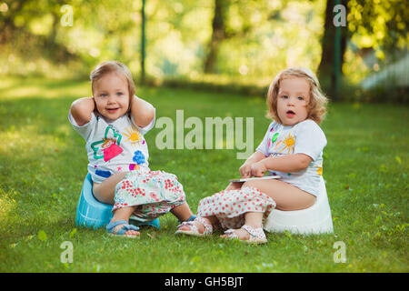 Die beiden baby wenig Mädchen sitzen auf Töpfe Stockfoto