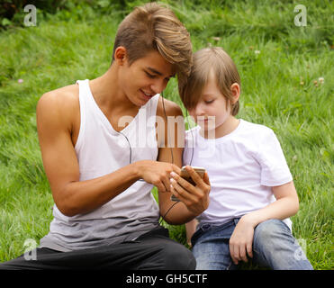 Senior und seinem jüngeren Bruder auf dem Rasen sitzen und auf das smartphone Stockfoto