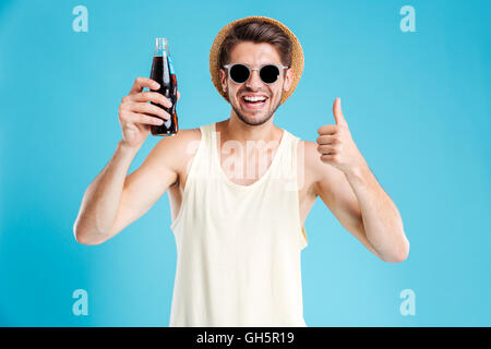Fröhlichen jungen Mann halten Flasche Soda nad zeigt Daumen hoch Stockfoto