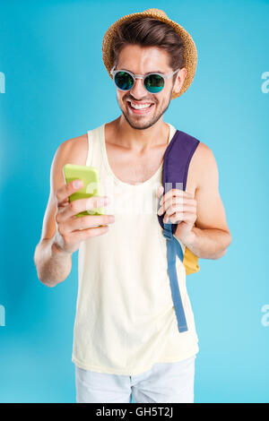 Fröhlichen jungen Mann in Hut und eine Sonnenbrille mit Rucksack mit Handy Stockfoto