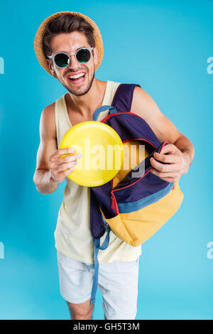 Fröhlichen jungen Mann in Hut und eine Sonnenbrille, die Einnahme von Frisbee-Scheibe von Rucksack Stockfoto