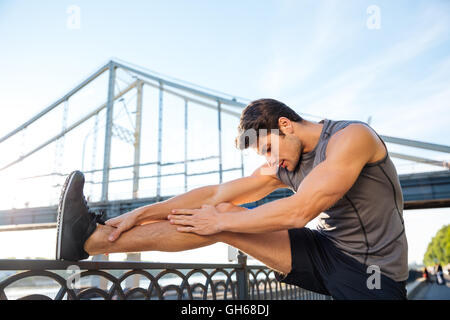 Hübscher Junge Sport Mann tut stretching gelehnt Brücke Geländer im freien Stockfoto
