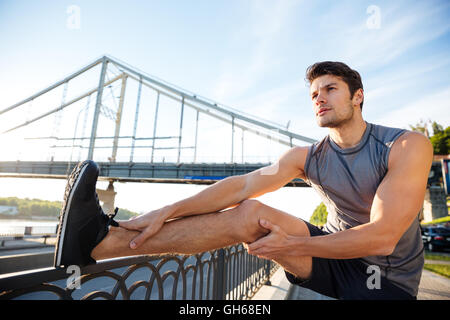 Hübscher Junge Sport Mann tut stretching gelehnt Brücke Geländer und wegschauen im freien Stockfoto