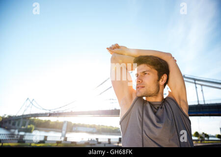 Hübscher Junge Sport Mann tut erstreckt sich auf das Brückengeländer und wegschauen im freien Stockfoto