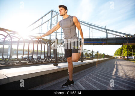 Hübscher Junge Sport Mann tut stretching gelehnt Brücke Geländer und wegschauen im freien Stockfoto