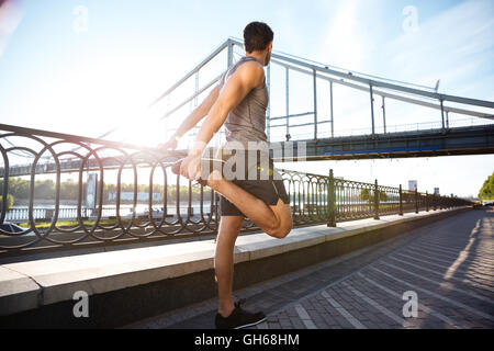 Seitenansicht eines schönen jungen Sport Mannes tun stretching gelehnt Brücke Geländer im freien Stockfoto