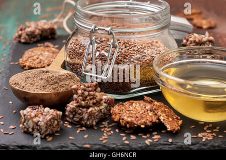 Leinsamen und Erzeugnissen: Leinöl, Leinsamen Mehl, Energieriegel und Cracker aus Flachs Samen auf einem dunklen steinigen Hintergrund Stockfoto