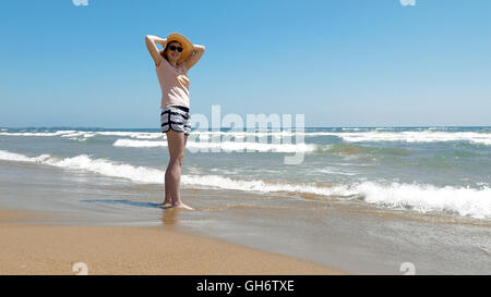 Frau steht am Strand mit Jute Hut auf Stockfoto