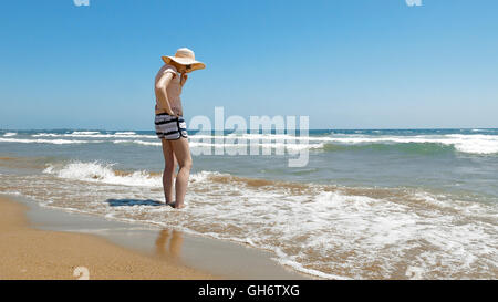 Frau steht am Strand mit Jute Hut auf Stockfoto