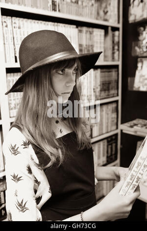 Sepia Foto von einem 12-jährigen Mädchen trägt einen schwarzen Hut in einem Comic-Buch-Speicher mit 2 Manga-Büchern Stockfoto