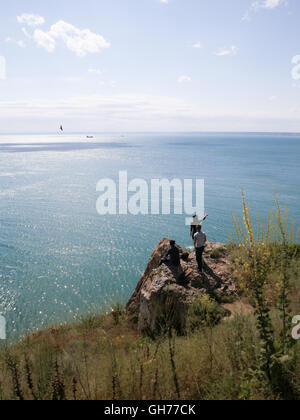 Drei junge Männer sitzen auf einem Felsen, Blick auf das Meer. Stockfoto