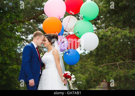 Junge Hochzeitspaar mit bunten Luftballons in den Kiefernwald umarmt Stockfoto