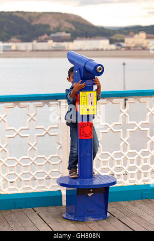 Ein kleiner Junge spielt Versteckspiel hinter ein Teleskop auf dem Llandudno Pier, Wales, UK Stockfoto