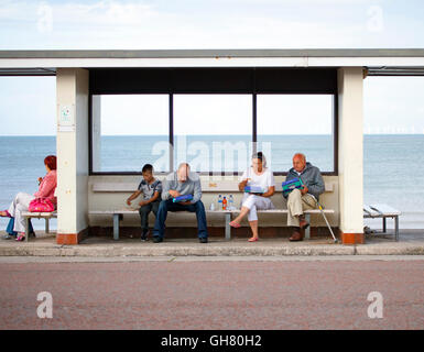 Einen warmen Sommerabend in Llandudno mit Besucher genießen den Abend im Resort, wie sie ihr von Fish &amp; Chips unter einem der Promenade Schutzhütten Abendessen Stockfoto