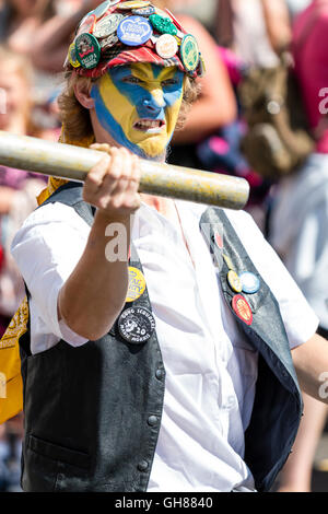 In der Nähe von Royal Liberty Morris Tänzerin, junger Mann, mit gelb und blau lackiert, trägt rote Kappe in Abzeichen abgedeckt, Fechten mit Metall Pol. Stockfoto