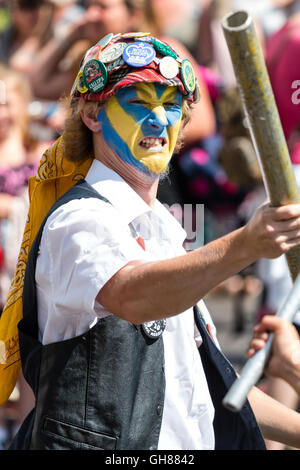 In der Nähe von Royal Liberty Morris Tänzerin, junger Mann, mit gelb und blau lackiert, trägt rote Kappe in Abzeichen abgedeckt, Fechten mit Metall Pol. Stockfoto