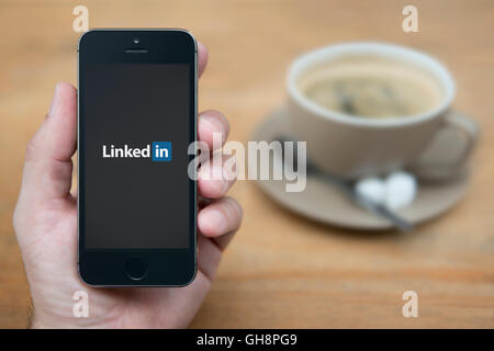 Ein Mann schaut auf seinem iPhone die Linkedin-Logo anzeigt, während bei einer Tasse Kaffee (nur zur redaktionellen Verwendung) saß. Stockfoto