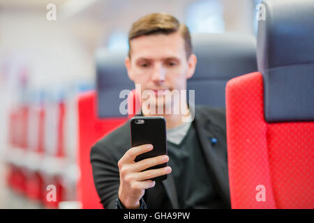 Junger Mann mit dem Zug reisen. Schreiben eine Nachricht auf Handy während der Fahrt mit dem Expresszug Tourist Stockfoto