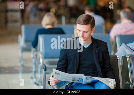 Kaukasischen Jüngling mit Zeitung am Flughafen beim Boarding warten. Lässige jungen Geschäftsmann tragen Jackett. Stockfoto