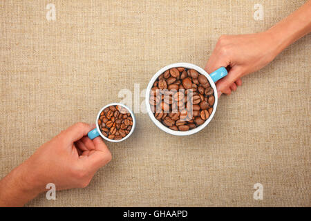 Zwei Hände, Mann und Frau, kleine und große Tassen voll mit gerösteten Kaffeebohnen über Leinwand Hintergrund zusammen zu halten Stockfoto