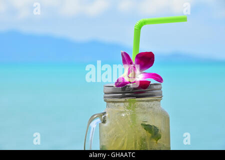 Große Gläser Becher Stil vollen Glas frisch gefrorenen Mojito mit Metallkappe Deckel, Stroh und lila Orchidee Blume im Café am Strand Stockfoto