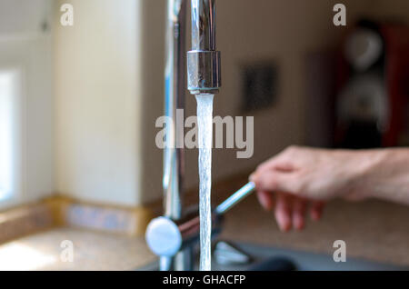 Frau Einschalten einen Wasserhahn mit fließendem Wasser und ein Chromhahn drinnen im Haus, Nahaufnahme von den Wasserstrahl Stockfoto