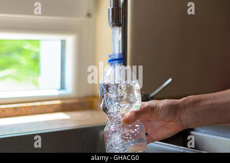 Frau eine Plastikflasche mit Wasser aus dem Wasserhahn in der Küche mit einer Nahaufnahme auf das fließende Wasser füllen Luftblasen Stockfoto