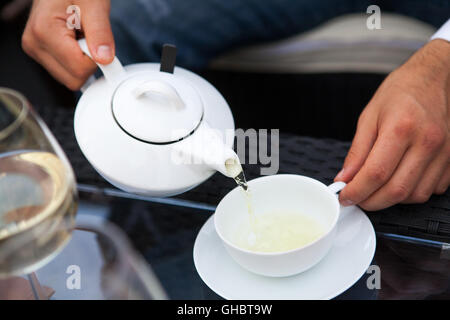 Man gießt in eine Tasse Tee aus einer Teekanne Stockfoto