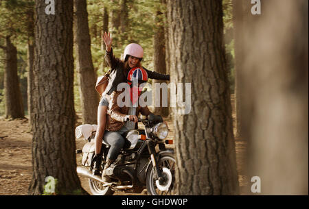 Ausgelassene junge Frau Motorrad im Wald Stockfoto