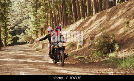 Ausgelassene junge Frau Motorrad auf Feldweg im Wald Stockfoto