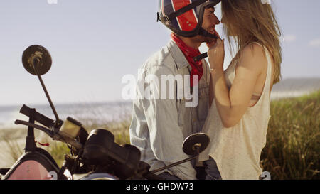 Liebevolle junge Paar am Motorrad mit Strand im Hintergrund Stockfoto