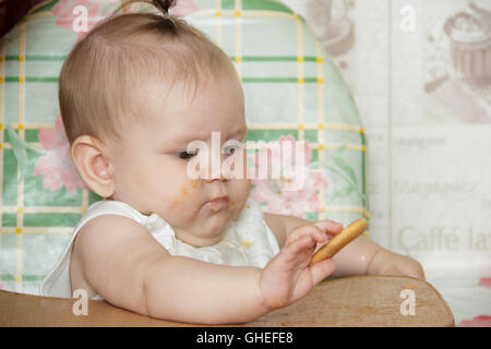 Kleines Kind Mädchen in einen Hochstuhl sitzt und isst cookies Stockfoto