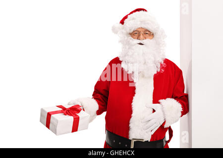 Santa Claus an eine Wand gelehnt und hält ein Geschenk isoliert auf weißem Hintergrund Stockfoto