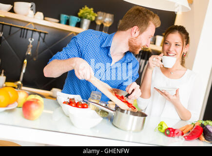 Frau trinkt Kaffee, während ein Mann eine Mahlzeit bereitet Stockfoto