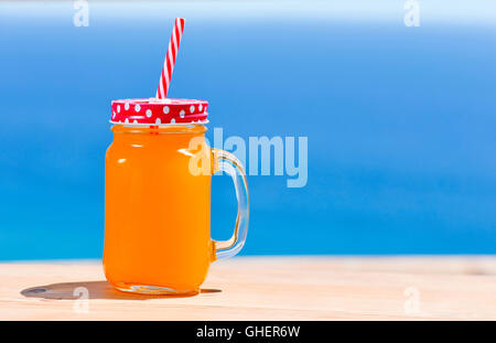 Closeup orange Getränk serviert in einem Glas Mason mit einem roten Deckel, gemustert mit weißen Punkten und rot-weiße Zeichnung Stockfoto