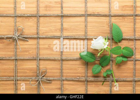 Platz gefüttert Seil Muster auf einem hölzernen Hintergrund und weiße rose mit Blättern zwischen es verwoben. Textur für Naturthemen. Stockfoto